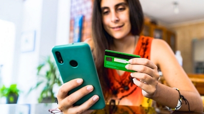 Persona usando una tarjeta de crédito y un teléfono móvil para hacer una compra.