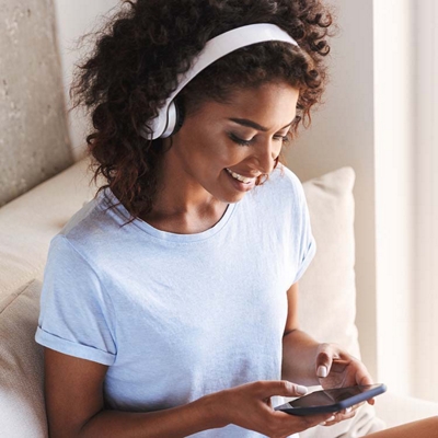 Mujer sentada usando audífonos y escribiendo en su teléfono.