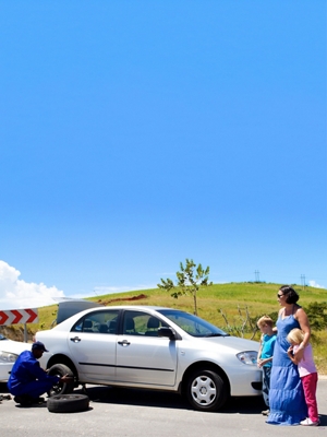 Una familia de pie junto a su auto mientras un empleado de AAA cambia un neumático